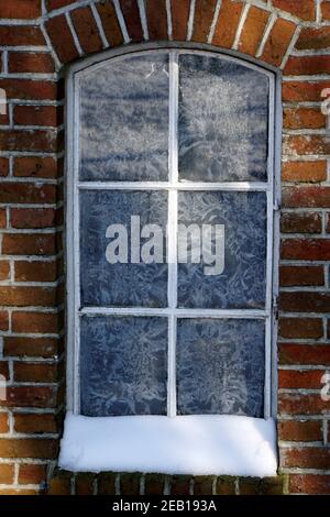 Old window in the winter. Ice crystals on the glass. Brick wall. Hoarfrost on the glass Stock Photo