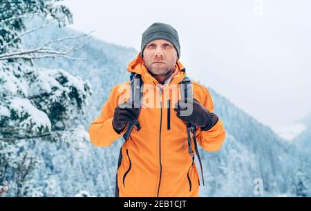 Man dressed bright orange softshell jacket with backpack have trekking on the winter mountains route. Active people or survival in the nature concept Stock Photo