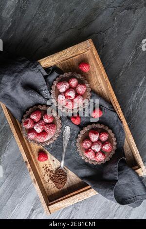 Cocoa crust tartlets filled with dark chocolate mousse made from whipped cream and raspberry puree, topped with fresh berries, sprinkled with powdered Stock Photo