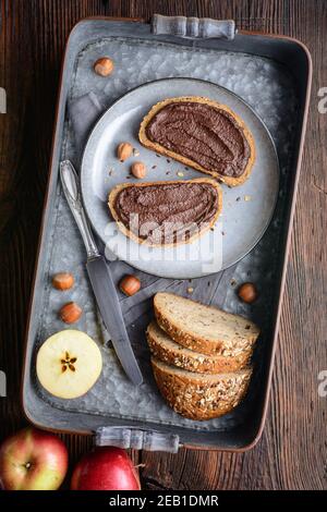 Healthy breakfast, slices of whole grain bread with apple spread made from cocoa powder, roasted ground hazelnuts and dark chocolate on rustic wooden Stock Photo