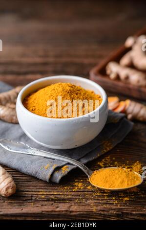 Anti-inflammatory food ingredient, turmeric powder in a ceramic bowl and fresh root on rustic wooden background Stock Photo