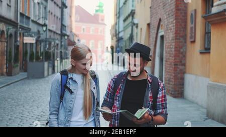 Two young tourists checking map while walking on main tourist street. They going sightseeing early in the morning. Stock Photo