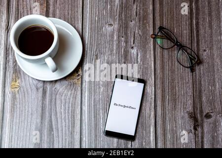 A mobile phone or cell phone laid on a wooden table with the New York Times app app open on screen Stock Photo