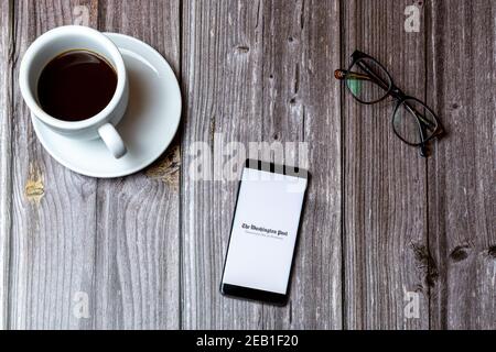 A mobile phone or cell phone laid on a wooden table with the Washington Post app open on screen next to a coffee Stock Photo