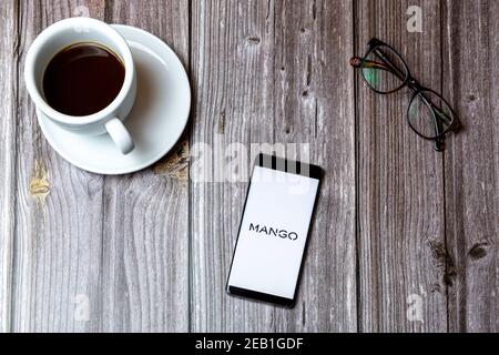 A mobile phone or cell phone laid on a wooden table with the Mango fashion app open on screen next to a coffee Stock Photo