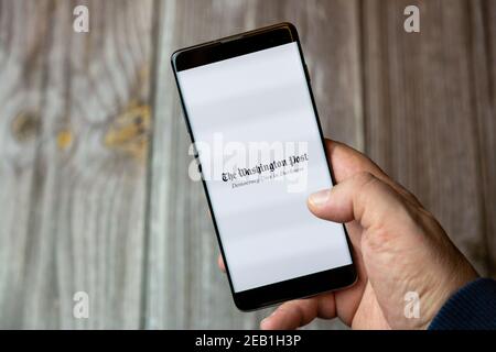 A mobile phone or cell phone being held by a hand with the Washington Post app open on screen Stock Photo