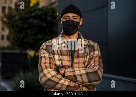Young handsome man walking on a street wearing a face mask to protect himself from the coronavirus Stock Photo