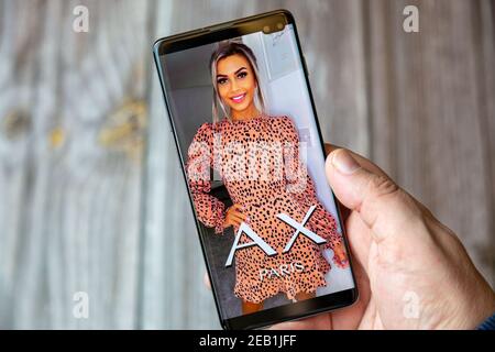 A mobile phone or cell phone being held by a hand with the AX Paris app open on screen Stock Photo