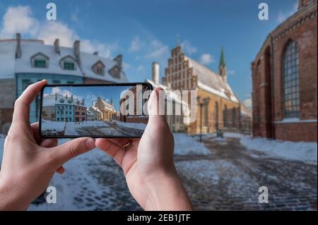 Tourist taking photo of snow-covered historical buildings near St. Peter's Church in winter in old town in Riga, Latvia. Stock Photo