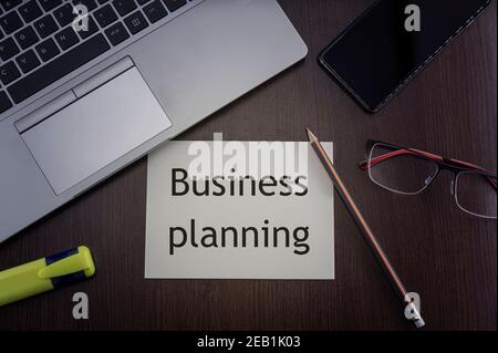 Business planning card. Top view of office table desktop background with laptop, phone, glasses and pencil with card with inscription business plannin Stock Photo