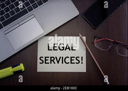 Legal services card. Top view of office table desktop background with laptop, phone, glasses and pencil with card with inscription legal services.  Bu Stock Photo