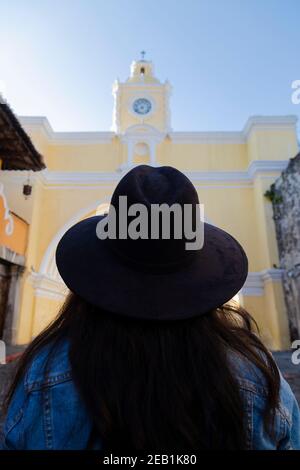 Young woman with hat looking towards the Arch of Santa Catalina in Antigua Guatemala - female traveler in main avenue of colonial city - famous monume Stock Photo