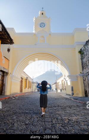 Young Hispanic woman walking under the Arch of Santa Catalina in Antigua Guatemala - tourist in important avenue of colonial Guatemala city with the W Stock Photo