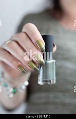 Woman's hand with long nails and light and dark green manicure with bottles of nail polish Stock Photo