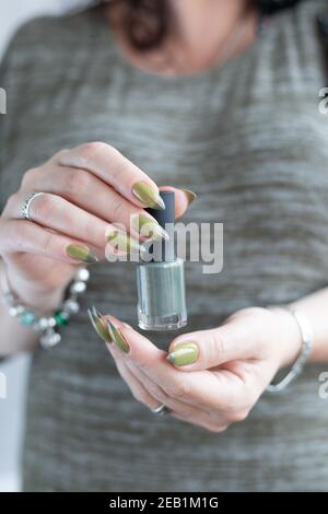 Woman's hand with long nails and light and dark green manicure with bottles of nail polish Stock Photo