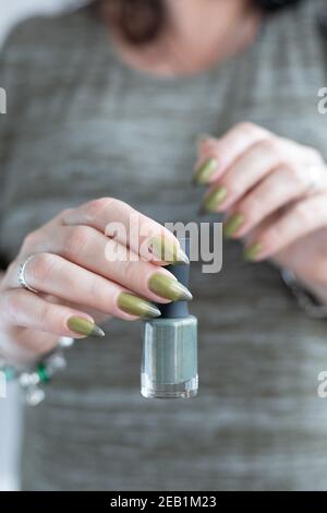 Woman's hand with long nails and light and dark green manicure with bottles of nail polish Stock Photo