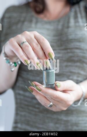 Woman's hand with long nails and light and dark green manicure with bottles of nail polish Stock Photo