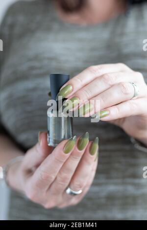 Woman's hand with long nails and light and dark green manicure with bottles of nail polish Stock Photo