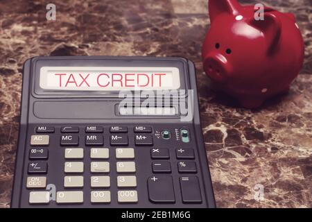 Tax credit. The text on the screen of the calculator lying next to the piggy bank on the table. Claiming the return of deductions. Return concept Stock Photo
