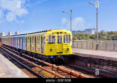 A bright yellow metro train departs from the platform and rushes along the metro bridge in Kyiv to the left side of the city. Stock Photo