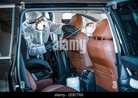 Disinfectant worker in protective mask and suit making disinfection of car seats Stock Photo