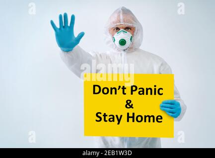 Healthcare worker showing stop gesture, holds paper with text 'Don't panic & Stay home' Stock Photo