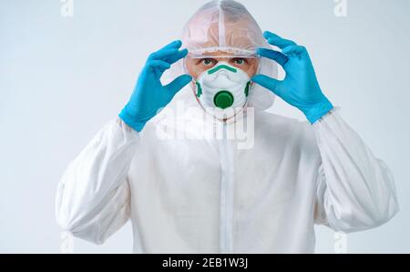 Healthcare worker in protective suit and medical mask puts on glasses. Health care concept. Stock Photo