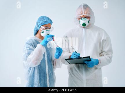 Doctor holds clipboard and nurse shows blood test result. Healthcare workers in protective suits and medical masks Stock Photo