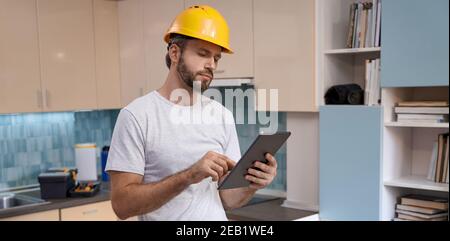 Builder in helmet working with tablet on kitchen background Stock Photo