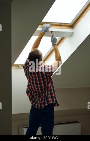 Helping you to fix it. Rear view of handyman using screwdriver while fixing or installing a window in a new dry wall attic Stock Photo