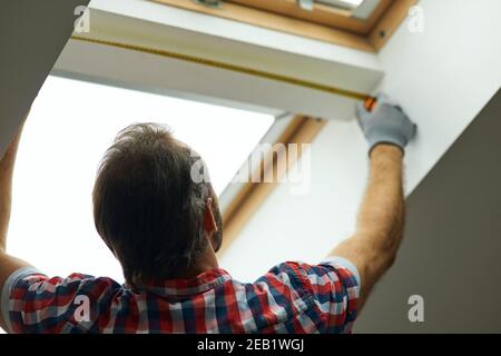 Close up shot of handyman using measure tape while measuring a window in a new dry wall attic Stock Photo