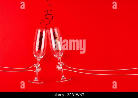 Two champagne glasses with red heart shaped confetti over red background. Festive mood. Overhead view, copy space. Celebration party concept Stock Photo