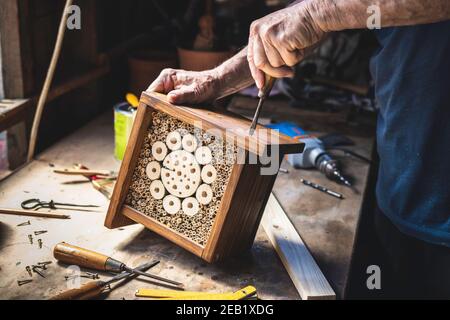 Man making wooden insect hotel. Craftsperson working in his workshop. Carpenter using screwdriver. Craft product Stock Photo