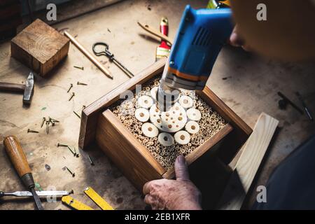 Craftsperson making wooden insect hotel. Carpenter using drill in workshop. Manual worker doing decorative insect house Stock Photo