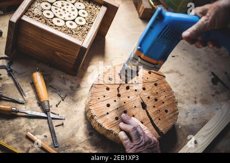 Craftsperson making wooden insect house. Carpenter using drill in workshop. Manual worker doing decorative insect hotel Stock Photo