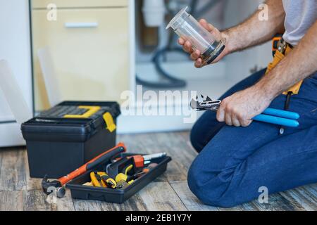 Plumbing done right. Cropped shot of professional plumber using pipe wrench and other tools while fixing sink pipe in the kitchen Stock Photo