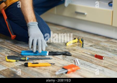 Tools to succeed. Close up of hand of repairman, professional plumber choosing the best tool for fixing a sink. Tools and equipment on the floor in Stock Photo