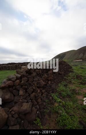 Vertical shot of stone fence formation in the field on background the cloudy sky over a mountain Stock Photo