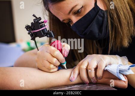 Woman tattoo master tattooing female hand at studio. Creative occupation Stock Photo