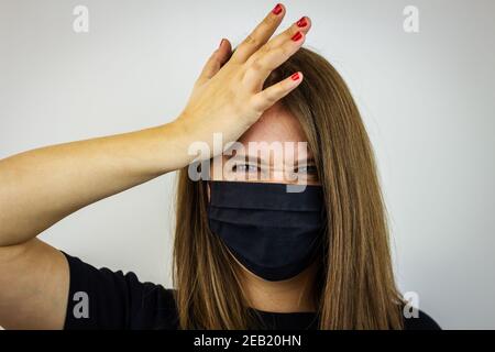 Portrait of young woman with face mask stressed by coronavirus pandemic. Front view face of a brunette who has a headache. Symptom of illness Stock Photo