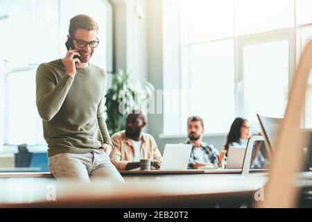 Joyful young office worker having a phonecall at workplace Stock Photo