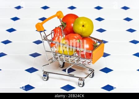 A shopping cart full of fruits and vegetables on the tiled floor. Stock Photo