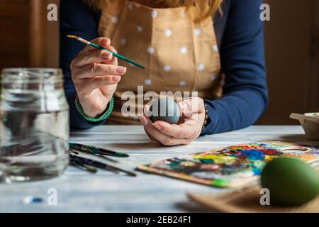 Woman is ready for painting easter eggs. Female artist wearing apron and holding colorful Easter egg for traditional religious holiday Stock Photo