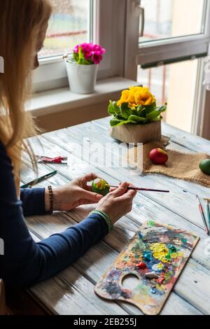 Woman coloring Easter eggs on white wooden table at home. Art and craft concept with real people. Homemade decoration. Preparation for tradition relig Stock Photo