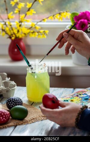 Creative painting Easter eggs at home. Woman cleaning paintbrush during coloring egg. Preparation for tradition religious celebration Stock Photo