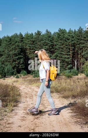 Woman hiker with backpack walking on footpath in nature. Female tourist hiking outdoors during summer day alone Stock Photo