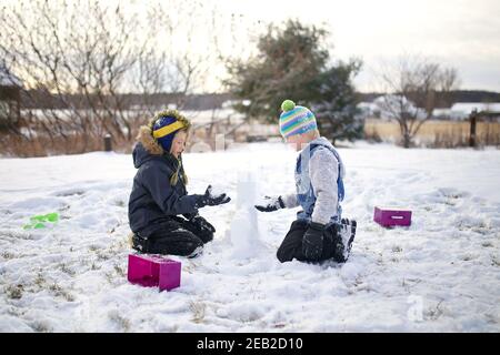 Two little boy children are playing outside in the winter snow, trying to build a fort. Stock Photo