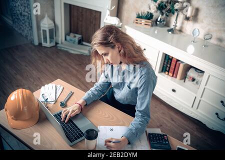 Engineer or Architect Worker Woman is Working at Home Workplace, Portrait of Female Engineer Using CAD on Laptop While Sketch Drawing on Blueprint at Stock Photo