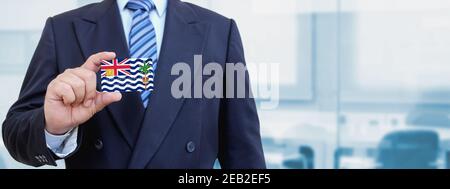 Cropped image of businessman holding plastic credit card with printed flag of British Indian Ocean. Background blurred. Stock Photo