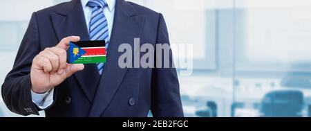Cropped image of businessman holding plastic credit card with printed flag of South Sudan. Background blurred. Stock Photo